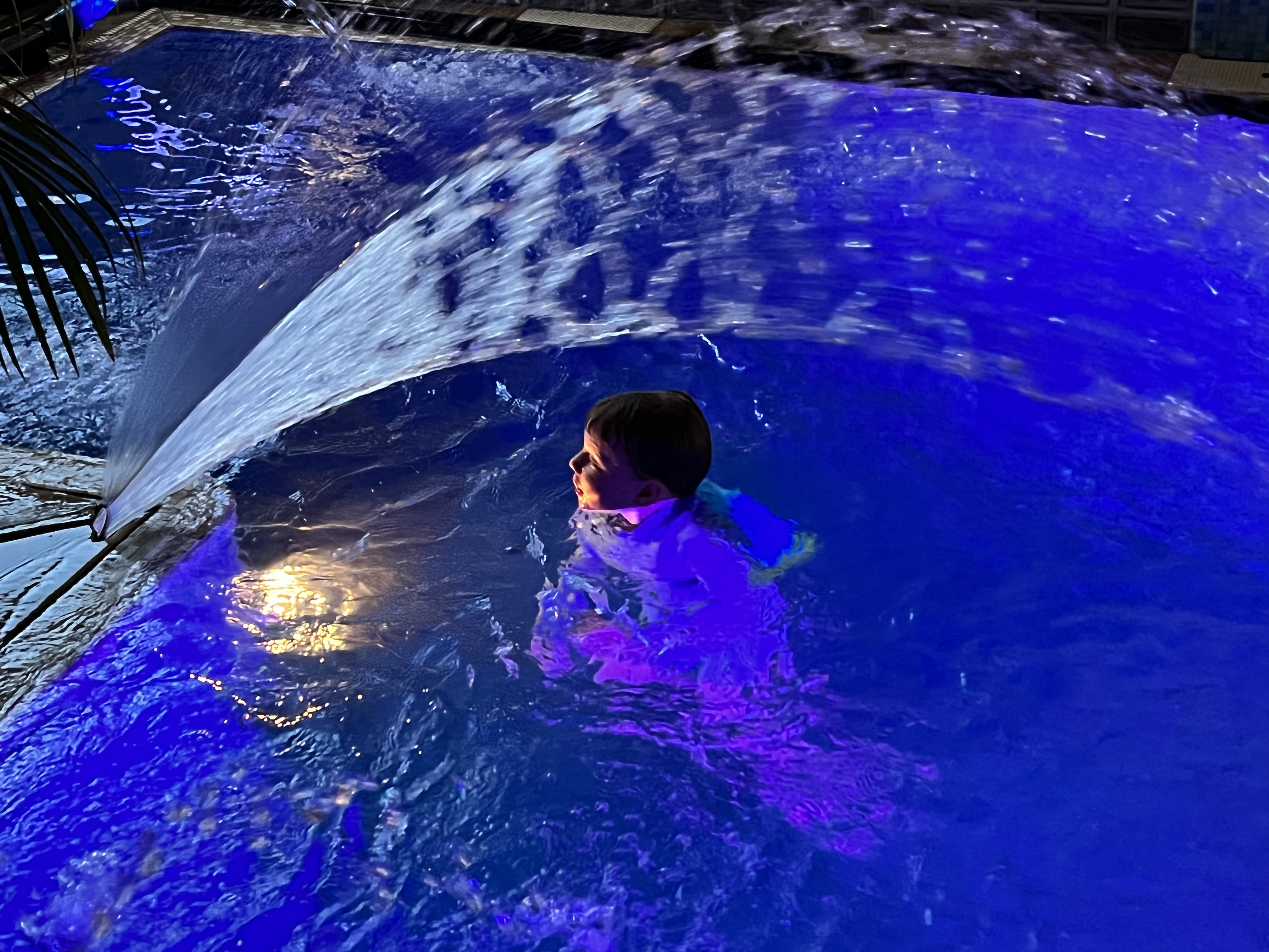A child enjoying a beautifully lit swimming pool at night
